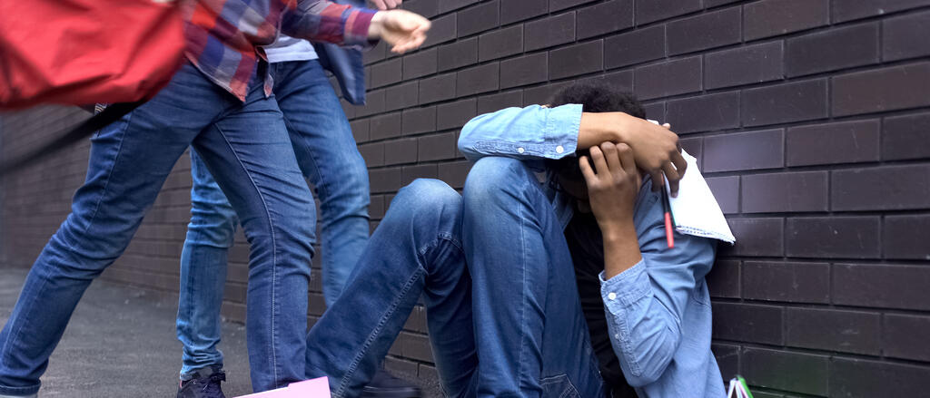 Zwei Schüler bedrohen ein drittes am Boden sitzendes Kind