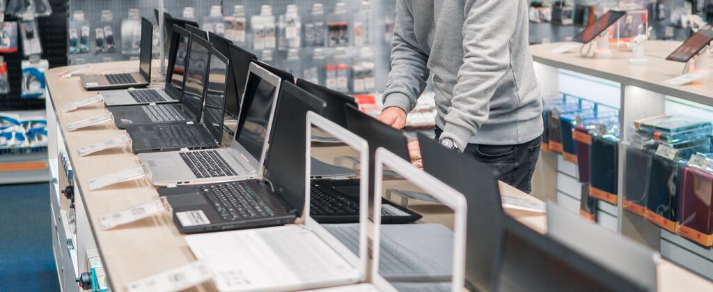 Ein Mann steht in einem Elektronikmarkt vor einer Reihe unterschiedlicher Laptops.