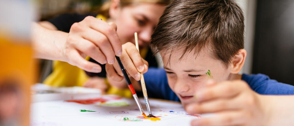 Eine Lehrerin erklärt einem Jungen mit Downsyndrom das Malen mit Farben