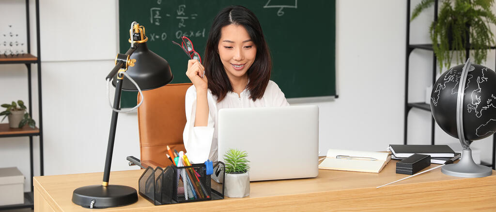 Eine Lehrerin sitzt an ihrem Schreibtisch vor einem Laptop.