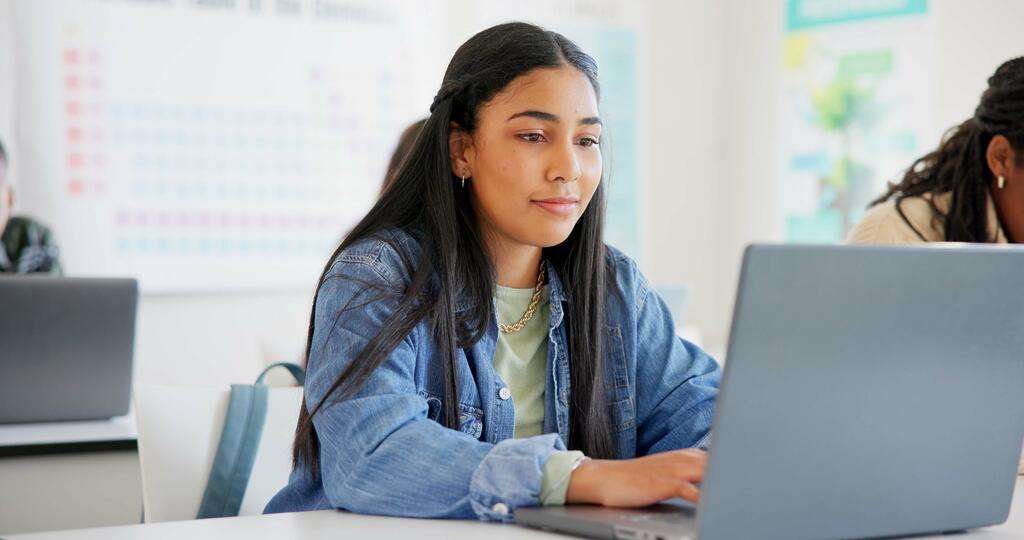 Eine Schülerin sitzt in einem Klassenzimmer und arbeitet an ihrem Laptop.