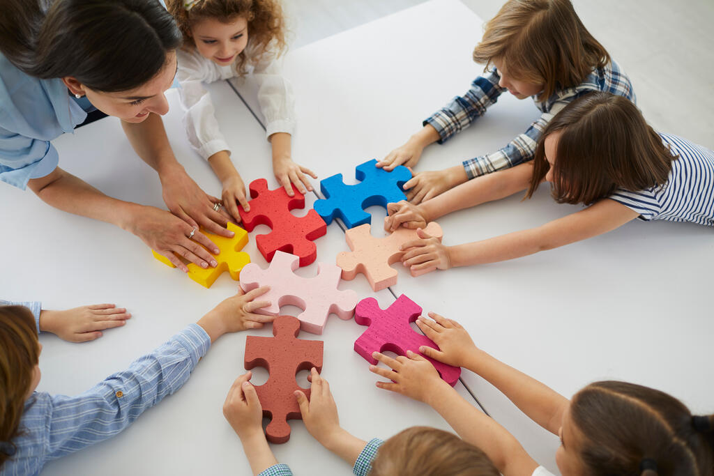 Lehrerin und Lerngruppe halten farbige Puzzleteile aneinander