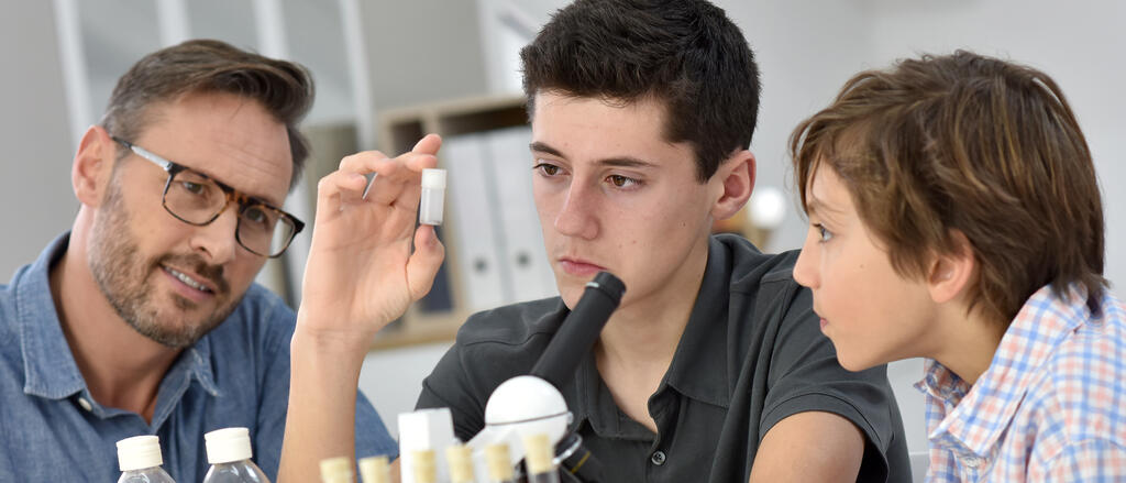 Eine Lehrkraft und zwei Schüler begutachten eine Probe.