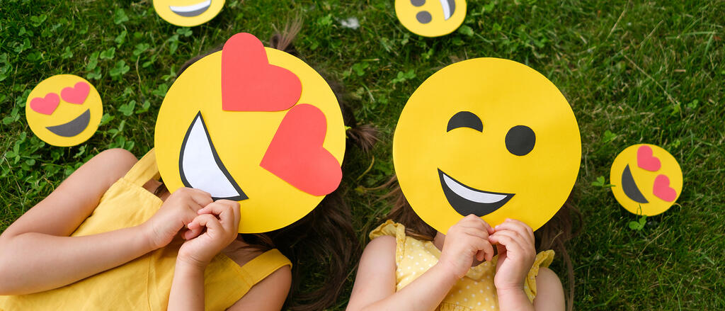 Zwei Kinder halten sich fröhliche Emoji-Motive vors Gesicht