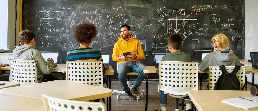 Lehrer sitzt mit einem Tablet vor vier Schülern im Klassenzimmer