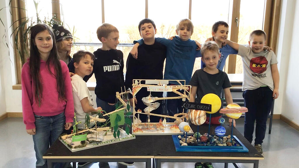Gruppenfoto mit Grundschülern. Davor ein Tisch mit den Gewinnermodellen der Achterbahnen.