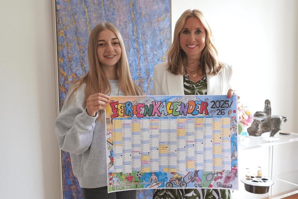 Links ist die diesjährige Gewinnerin Anna-Lena Erler zu sehen. Rechts steht Kultusministerin Anna Stolz. Beide halten den gedruckten Ferienkalender 2025/2026 in den Händen.