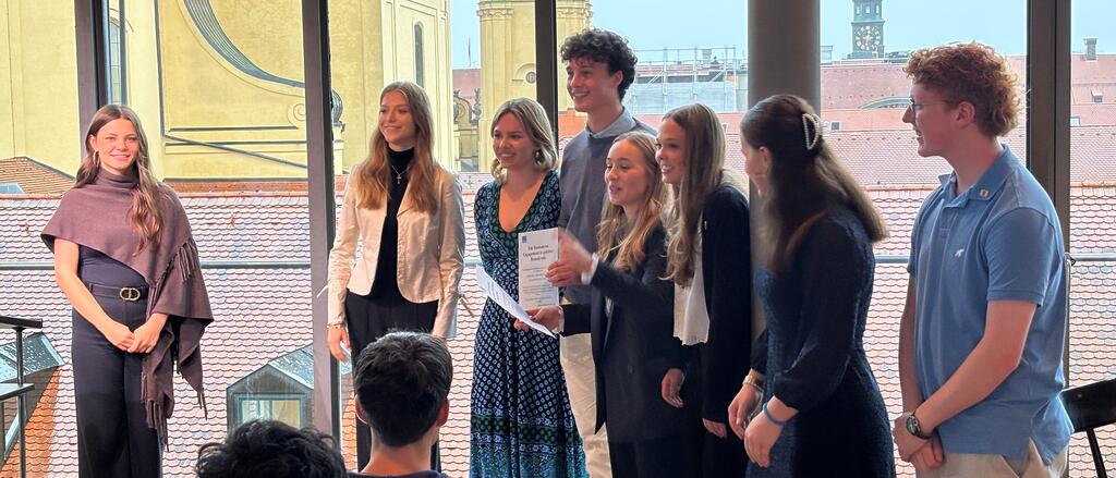 Schülerinnen und Schüler bei der Urkundenübergabe anlässlich der Auszeichnung zum Landeswettbewerb des Landesschülerrats „Werte leben – Demokratie bewegen! Zu sehen sind acht Jugendliche, hinter ihnen die Theatinerkirche. 