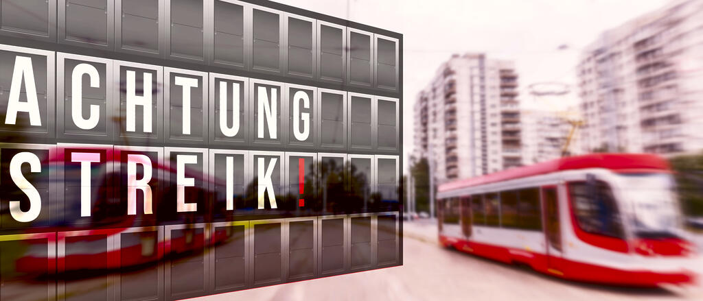 Busse unscharf im Hintergrund. Im Vordergrund eine Anzeigetafel mit der Aufschrift "Achtung Streik"
