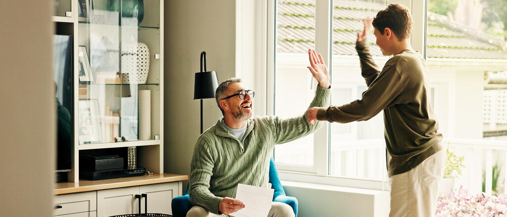 Vater im Sohn im Wohnzimmer klatschen ein. Vater hält das Zeugnis des Sohnes in der Hand